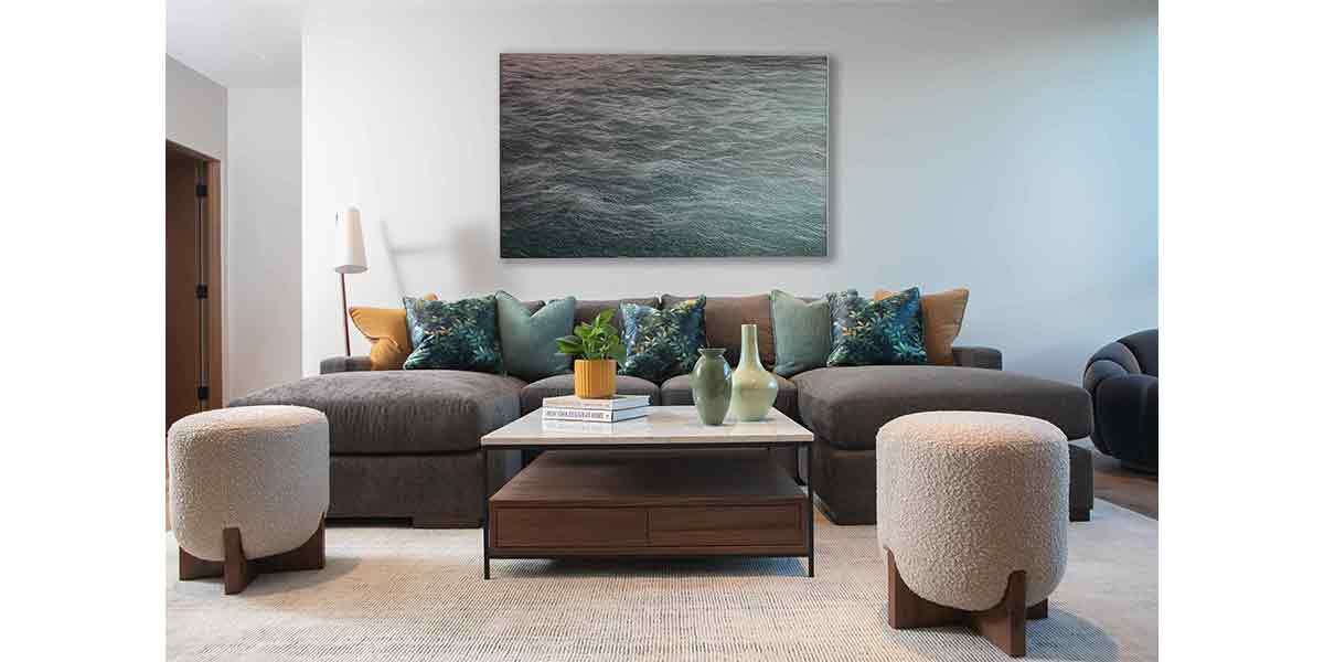 Stylish coastal living room with sofa, ottomans, and ocean artwork.