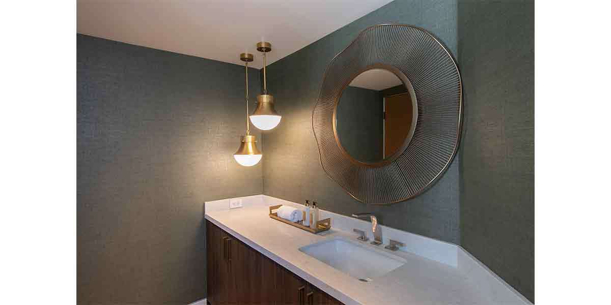 Contemporary bathroom with dark green textured walls, round mirror, and elegant pendant lights.