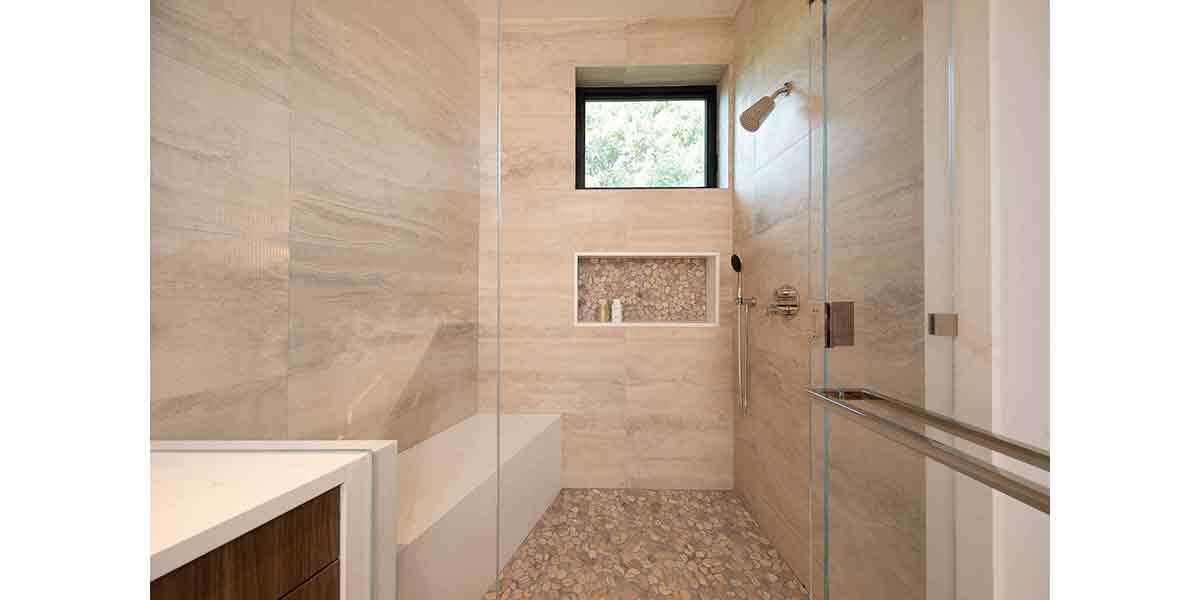 Modern beige tile walk-in shower with built-in niche and window for a sleek bathroom design.