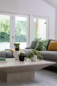 Modern living room with large windows, gray sofa, and green plants.