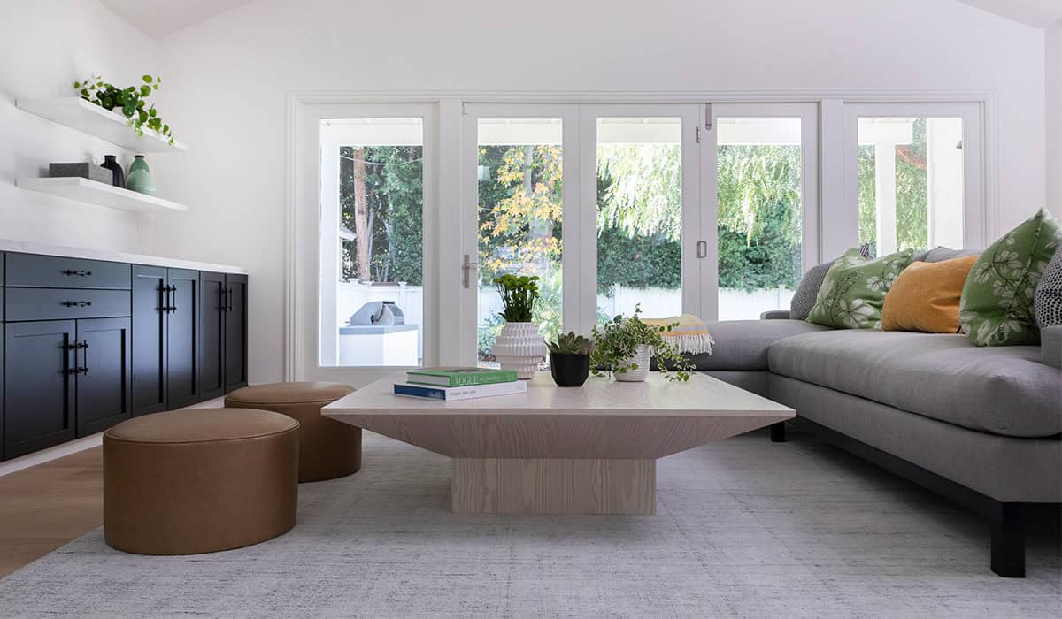 Bright modern living room with large windows, neutral furniture, and lush outdoor views.