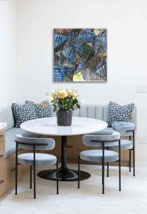 Contemporary dining space featuring a round table, blue upholstered chairs, and vibrant abstract wal.